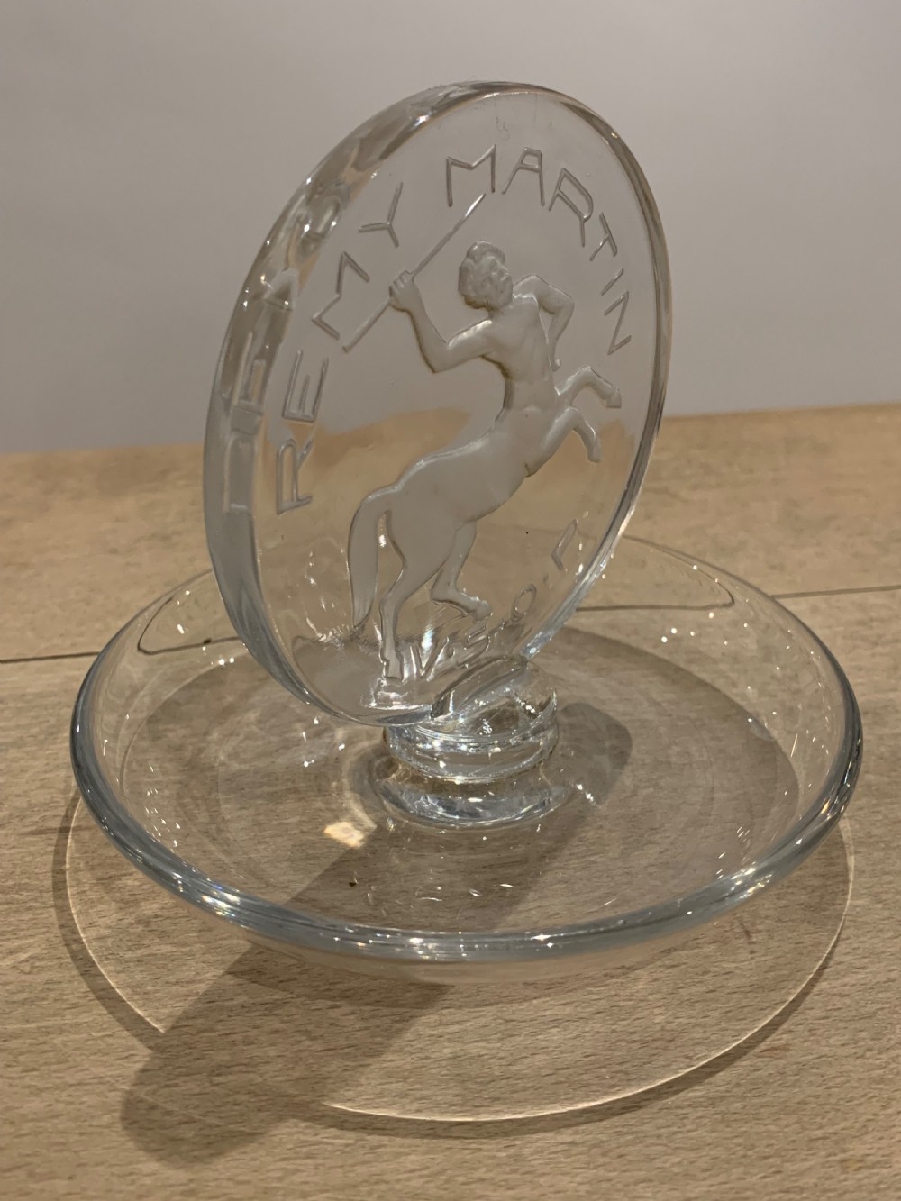 A clear glass Art Deco circular ashtray featuring an upright circular medallion with a frosted relief depicting a centaur holding a javelin above the lettering REMY MARTIN V.S.O.P. View II