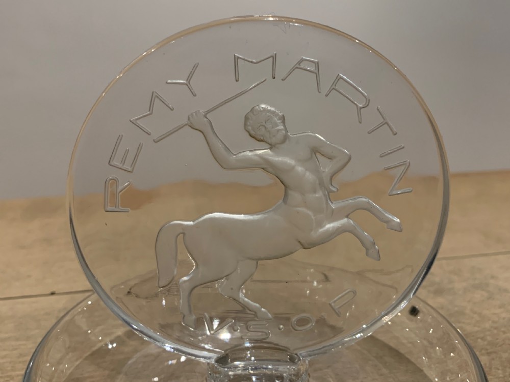 A clear glass Art Deco circular ashtray featuring an upright circular medallion with a frosted relief depicting a centaur holding a javelin above the lettering REMY MARTIN V.S.O.P. View IV