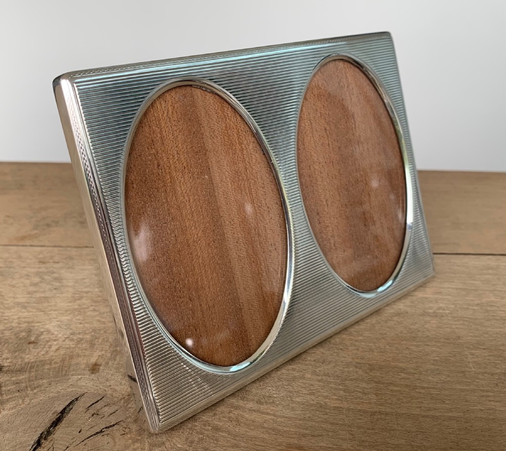 A rectangular sterling silver twin photo frame with linear engine-turned texturing and two oval apertures.