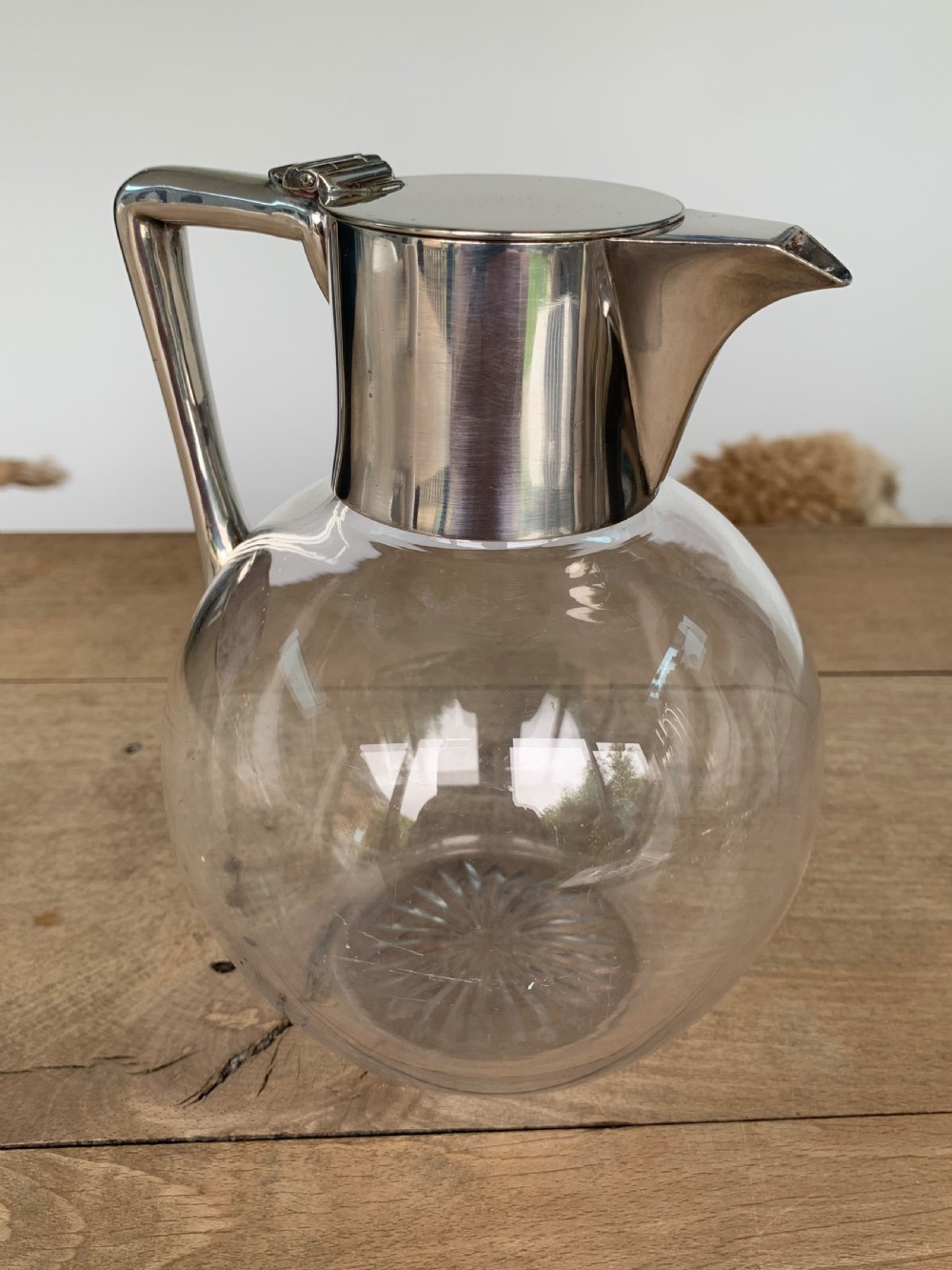 A clear spherical glass claret jug featuring a silver-plated collar, flat hinged cap, angular handle, and a cut starburst pattern on the base. View II