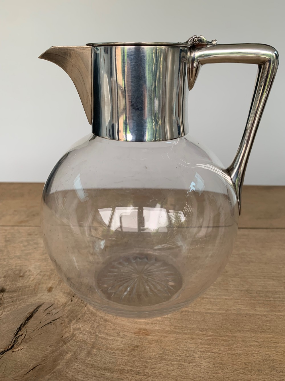 A clear spherical glass claret jug featuring a silver-plated collar, flat hinged cap, angular handle, and a cut starburst pattern on the base. View IV