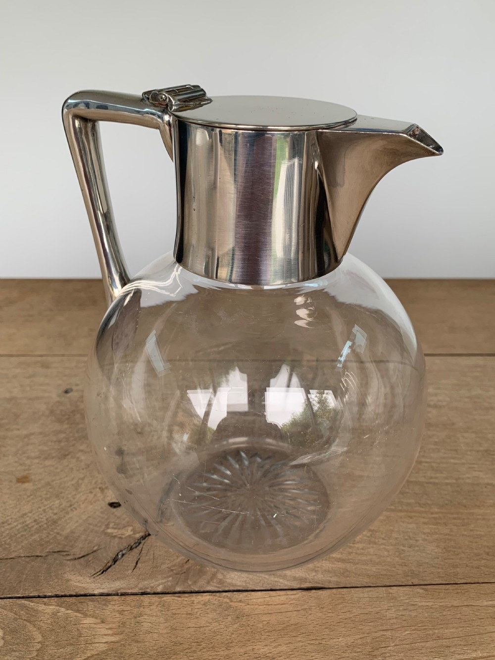 A clear spherical glass claret jug featuring a silver-plated collar, flat hinged cap, angular handle, and a cut starburst pattern on the base. View IX