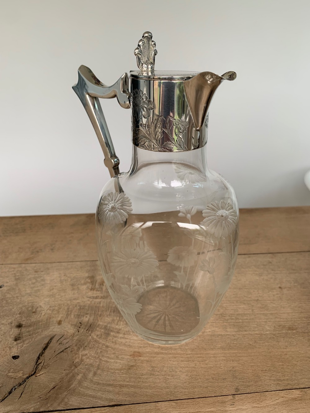 An Edwardian clear glass claret jug featuring wheel-engraved daisy motifs and a hallmarked sterling silver collar with handle. View II