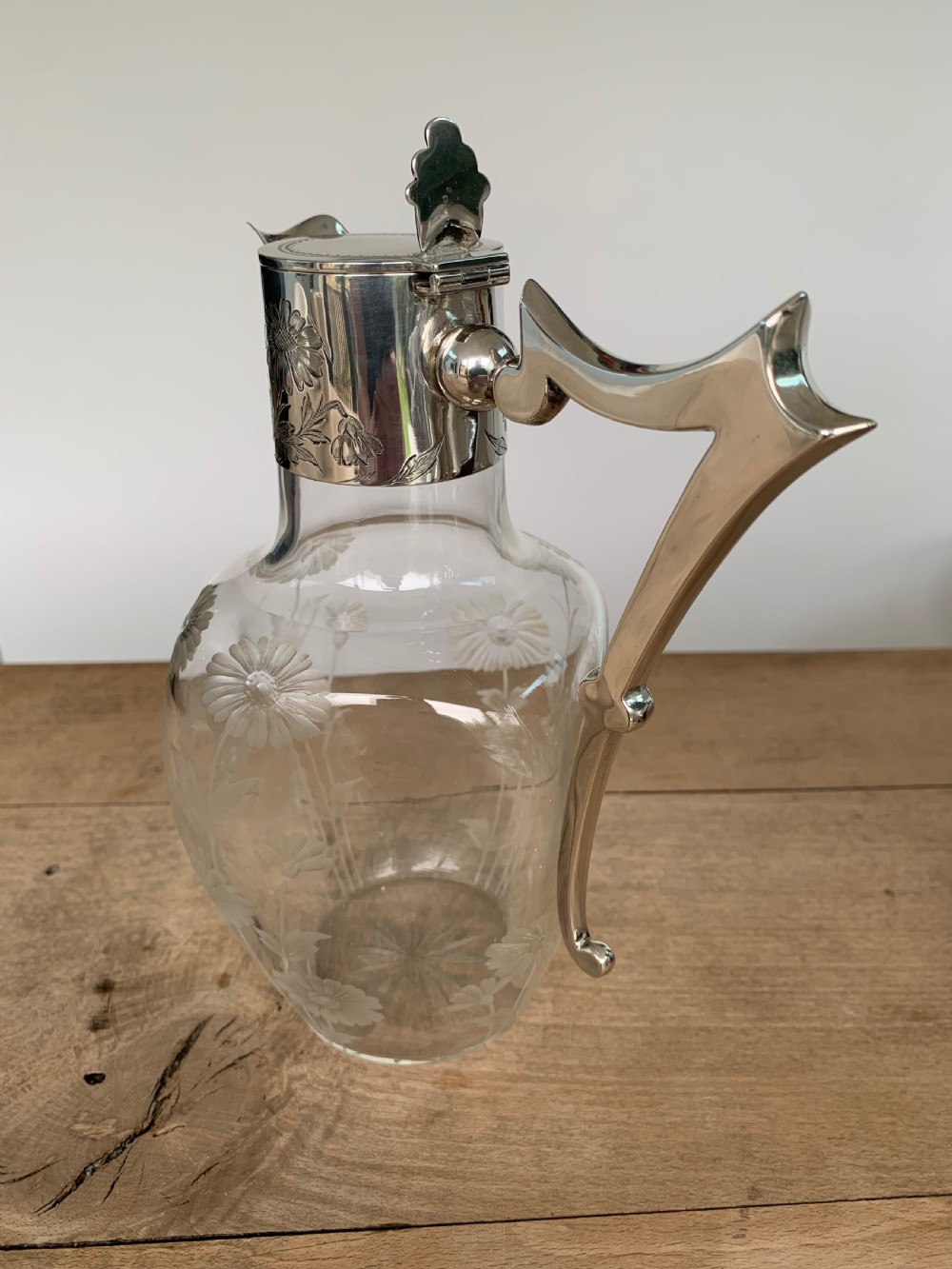An Edwardian clear glass claret jug featuring wheel-engraved daisy motifs and a hallmarked sterling silver collar with handle. View IV