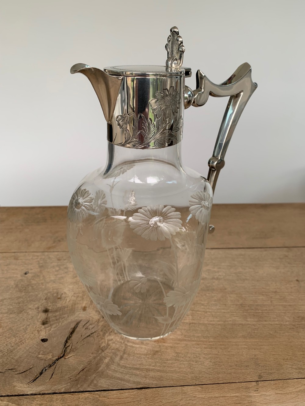 An Edwardian clear glass claret jug featuring wheel-engraved daisy motifs and a hallmarked sterling silver collar with handle. View V