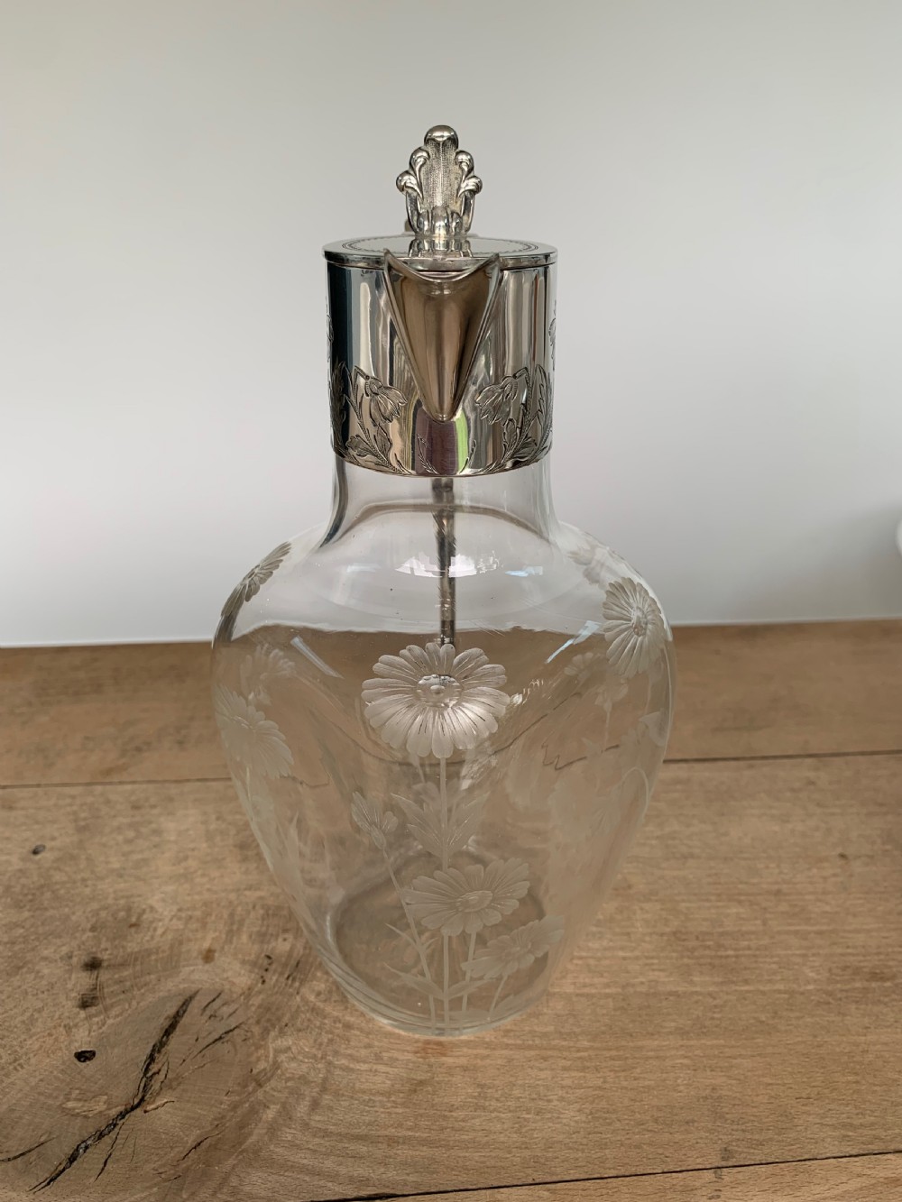 An Edwardian clear glass claret jug featuring wheel-engraved daisy motifs and a hallmarked sterling silver collar with handle. View VI