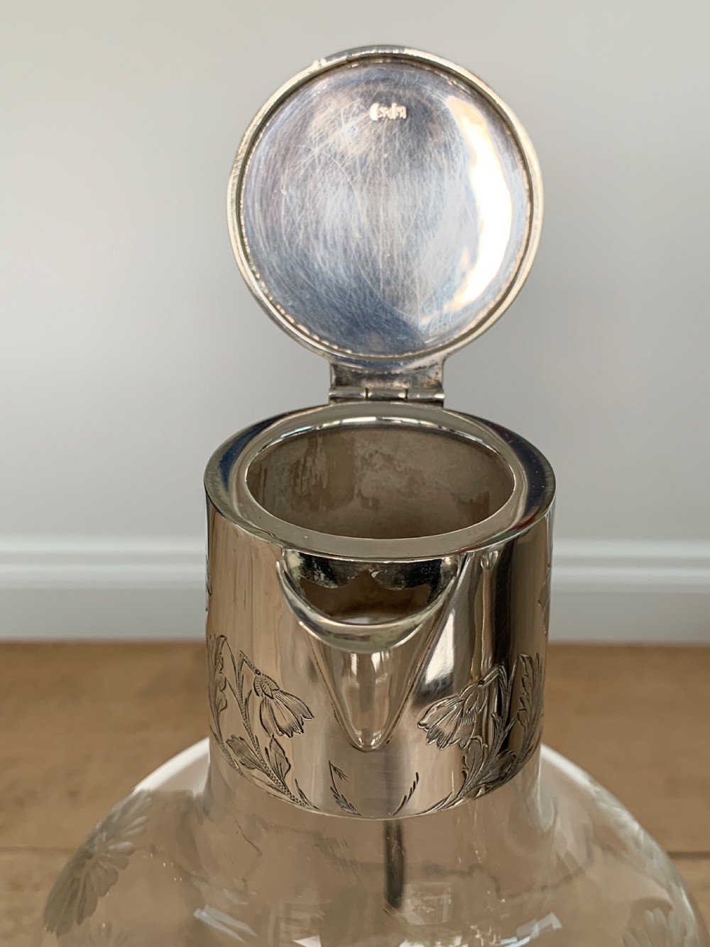 An Edwardian clear glass claret jug featuring wheel-engraved daisy motifs and a hallmarked sterling silver collar with handle. View X