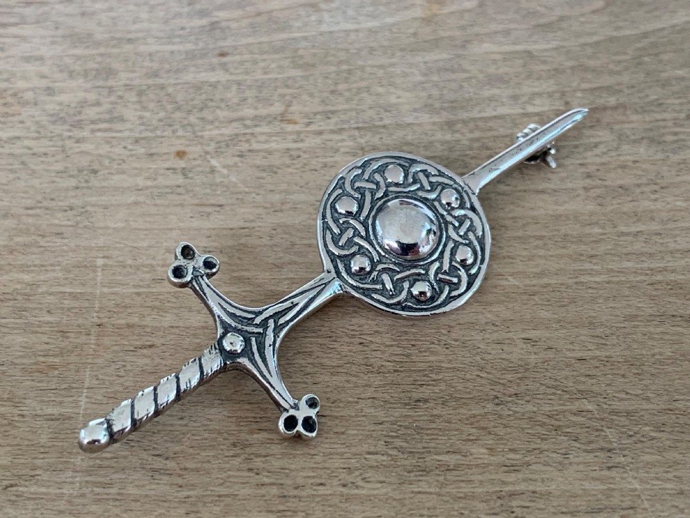 A sterling silver brooch designed in the shape of a sword passing through a circular shield embellished with intricate Celtic knotwork. View II