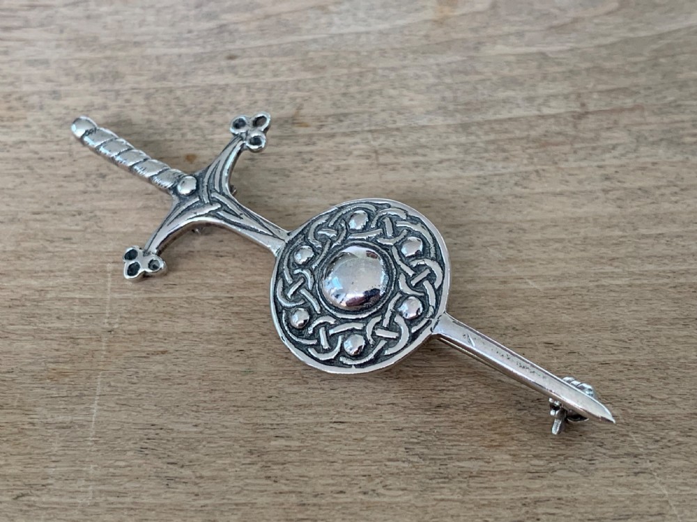 A sterling silver brooch designed in the shape of a sword passing through a circular shield embellished with intricate Celtic knotwork. View IV