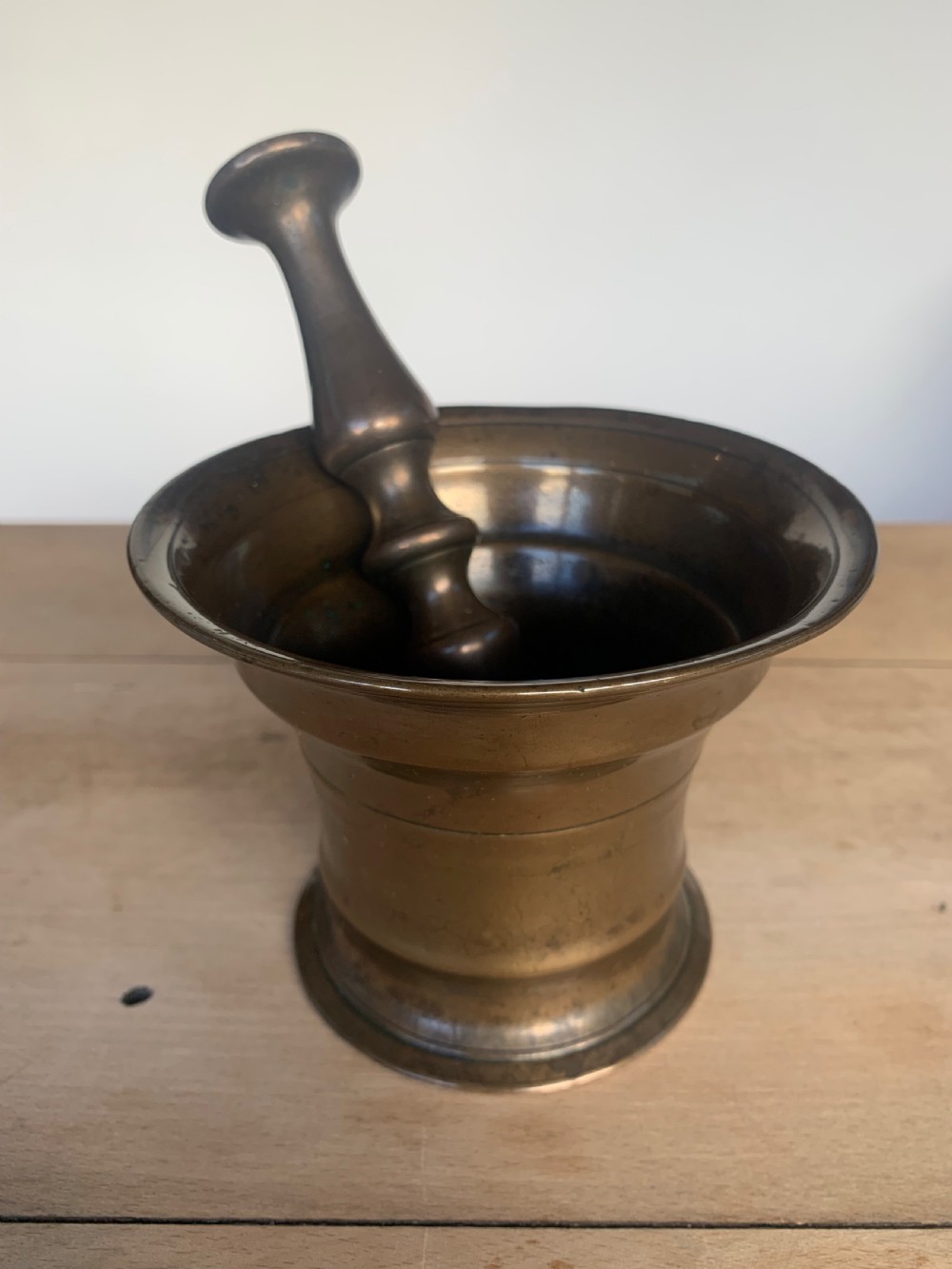 An antique cast bronze mortar with a flared rim and turned waist, accompanied by a matching metal pestle.