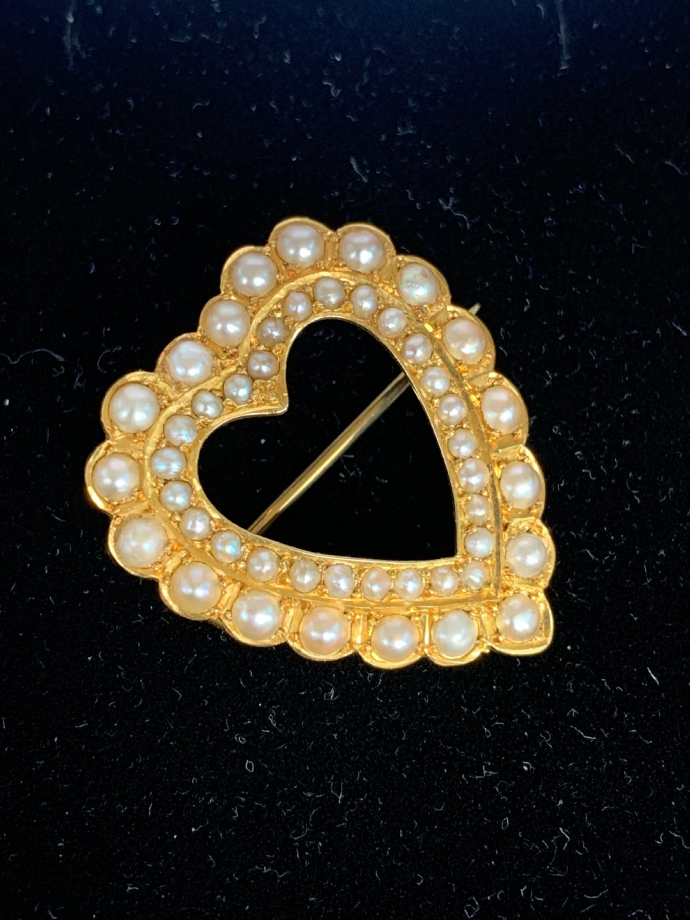 A Victorian 18ct yellow gold heart brooch featuring a double border of set seed pearls around an open centre. View IV
