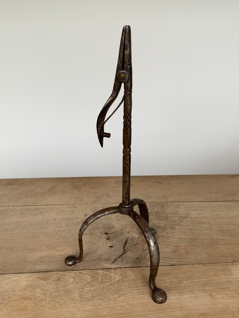 A hand-forged wrought iron rushlight holder featuring a sprung pincer clamp mechanism raised on a curved tripod base.