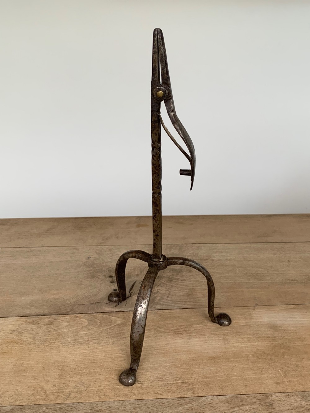 A hand-forged wrought iron rushlight holder featuring a sprung pincer clamp mechanism raised on a curved tripod base. View II