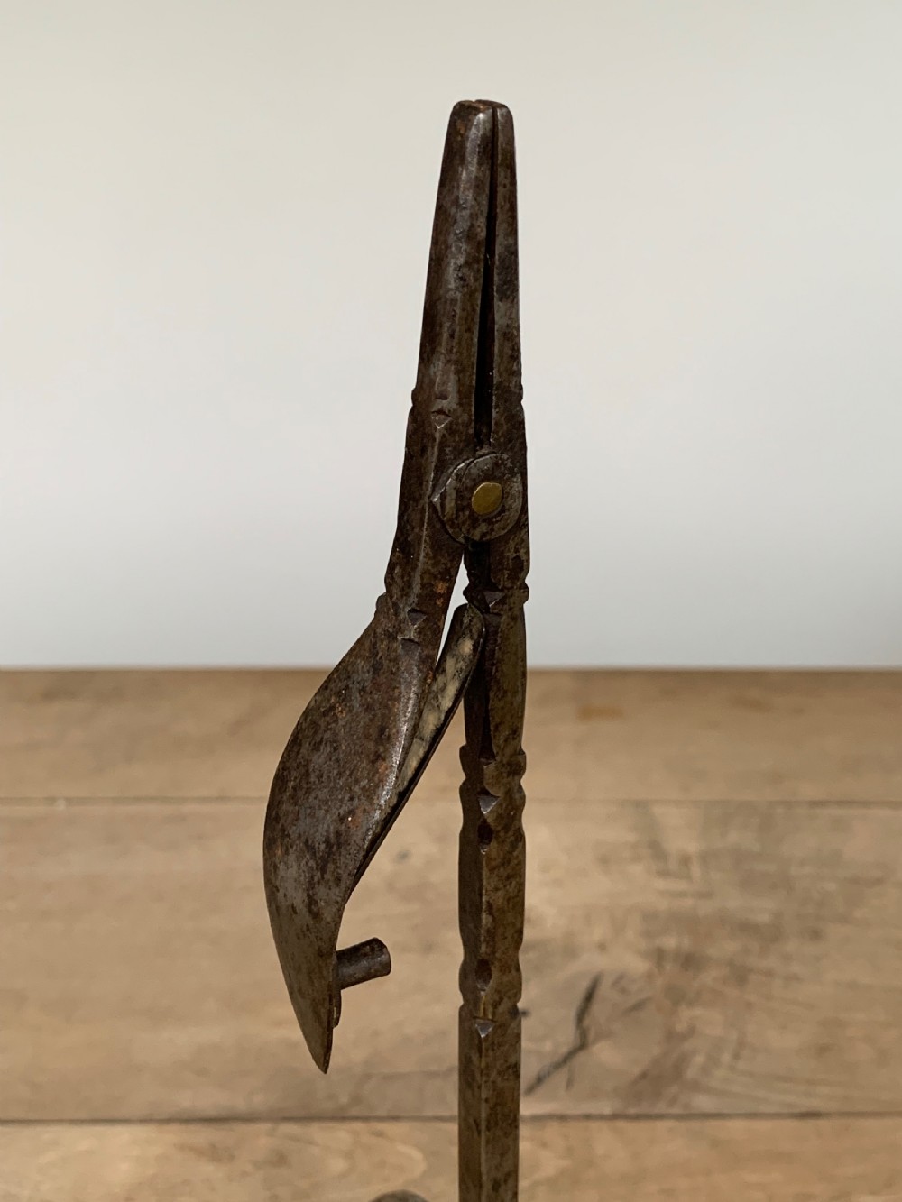 A hand-forged wrought iron rushlight holder featuring a sprung pincer clamp mechanism raised on a curved tripod base. View VIII