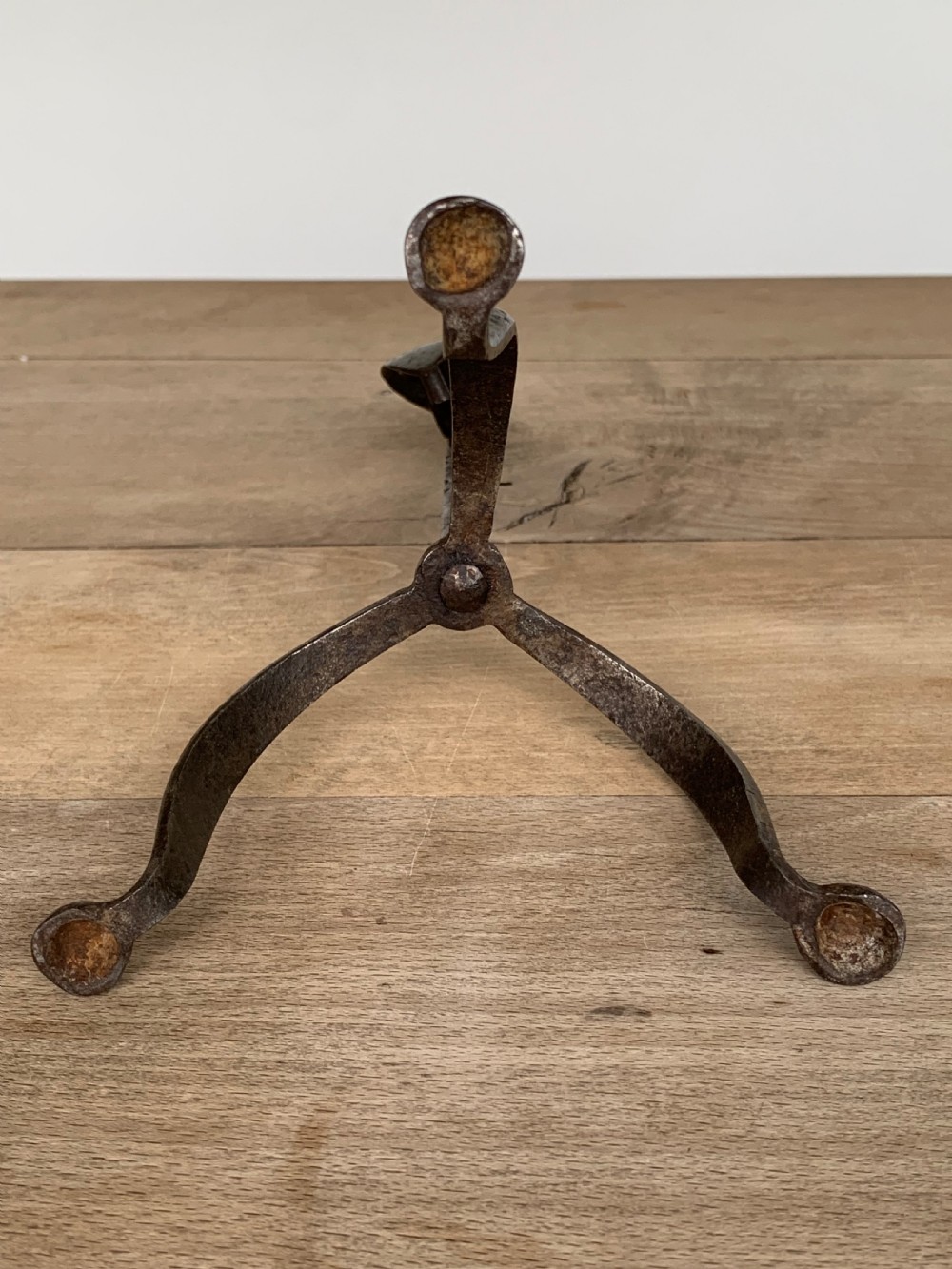 A hand-forged wrought iron rushlight holder featuring a sprung pincer clamp mechanism raised on a curved tripod base. View IX