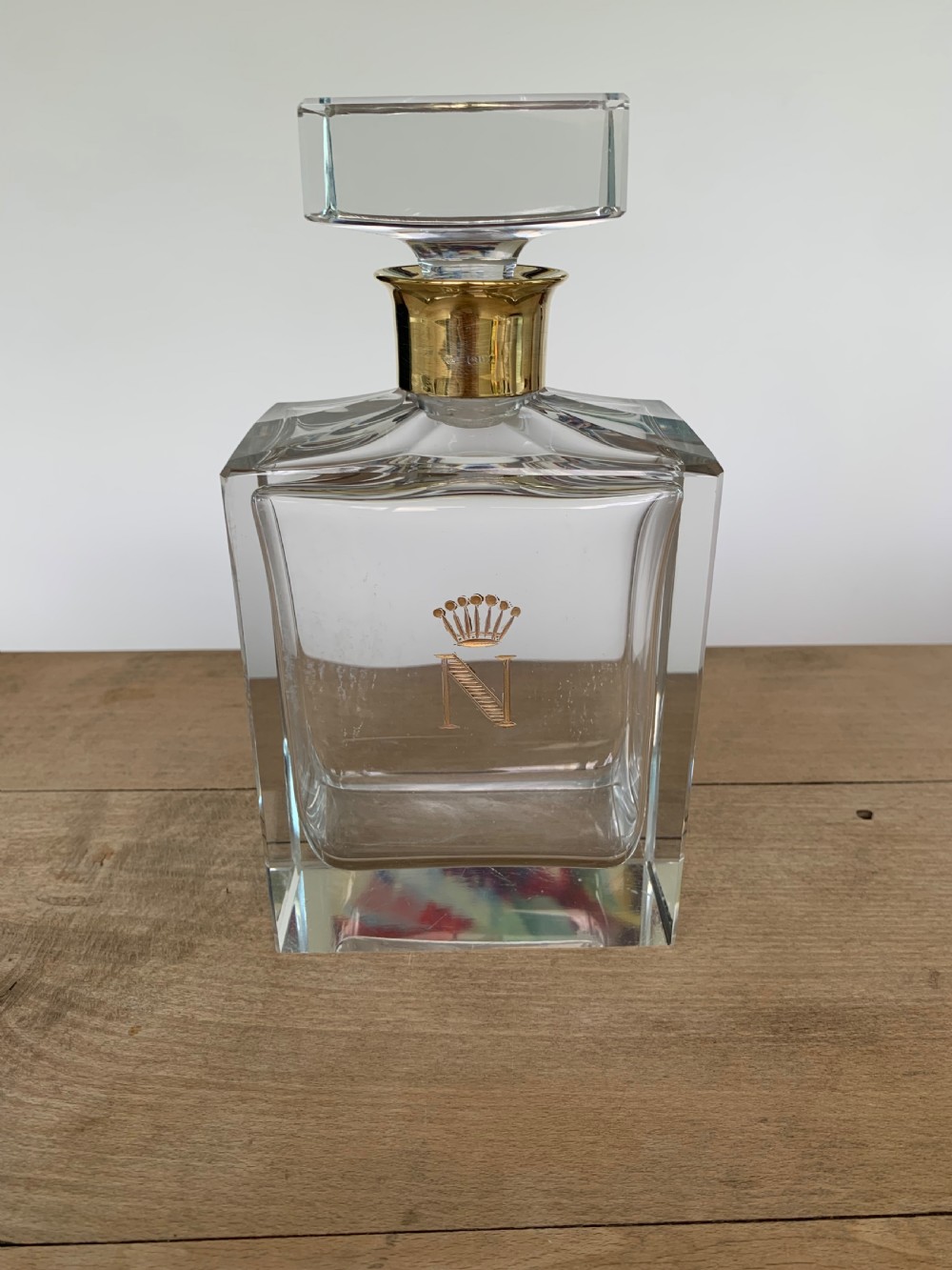 A square clear crystal brandy decanter featuring a silver-gilt collar around the neck, a crowned N monogram on the body, and a rectangular stopper.