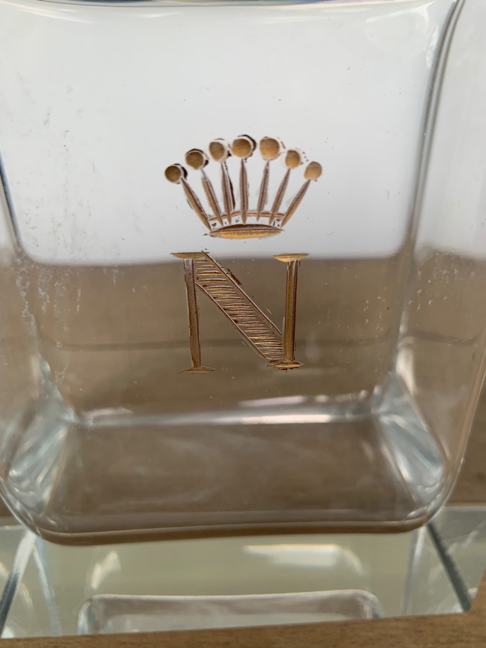 A square clear crystal brandy decanter featuring a silver-gilt collar around the neck, a crowned N monogram on the body, and a rectangular stopper. View IX