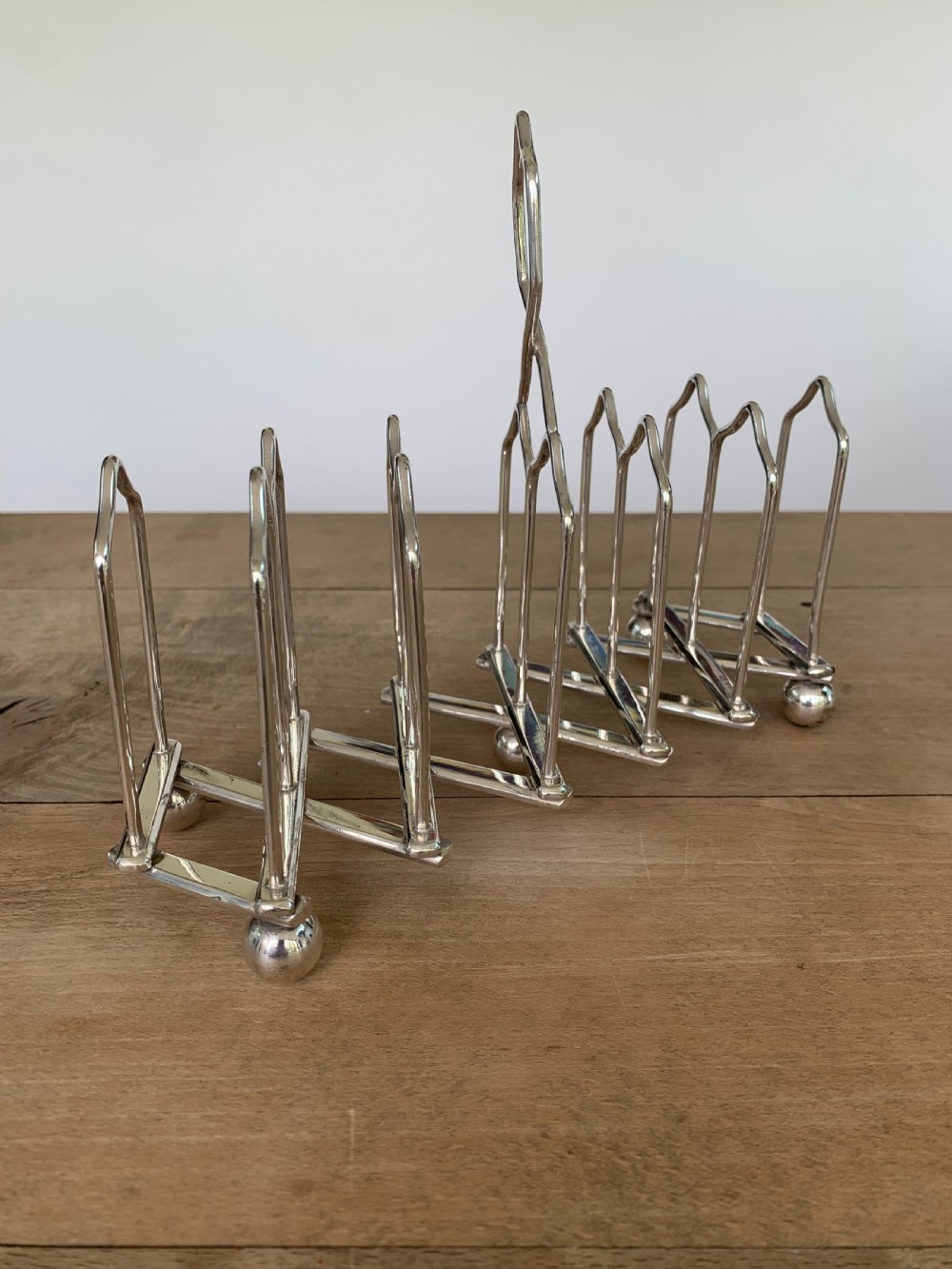 An expandable silver plated Victorian toast rack sits on a wooden surface, showing its collapsible metal frame and central loop handle.