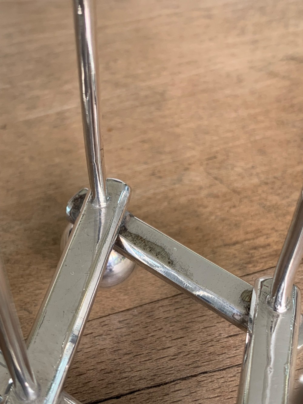 An expandable silver plated Victorian toast rack sits on a wooden surface, showing its collapsible metal frame and central loop handle. View XI