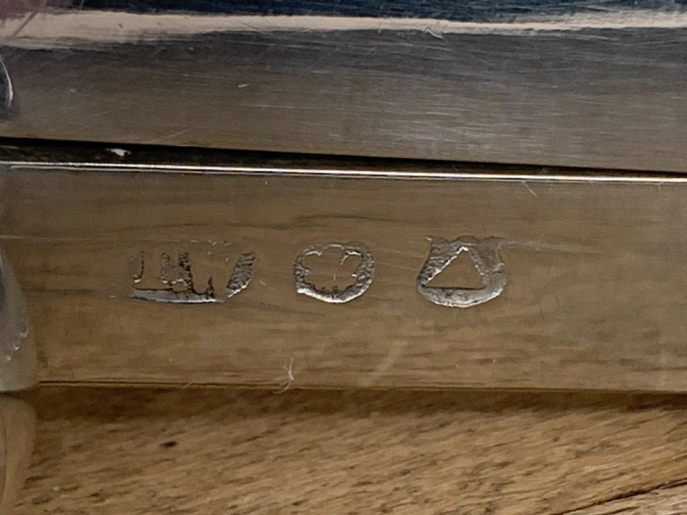 An expandable silver plated Victorian toast rack sits on a wooden surface, showing its collapsible metal frame and central loop handle. View XII