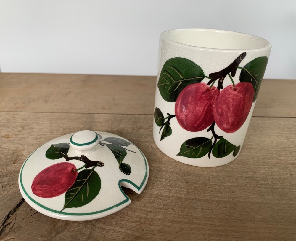 A lidded white ceramic preserve pot decorated with hand-painted red cherries and green leaves, featuring a notch for a spoon. View II