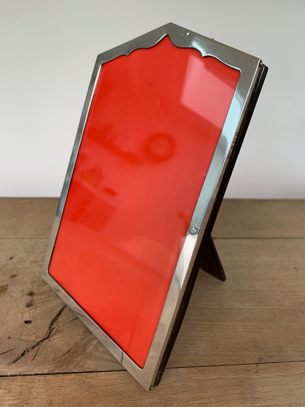 An Art Deco sterling silver picture frame featuring an arched top edge and a bright red background insert. View II