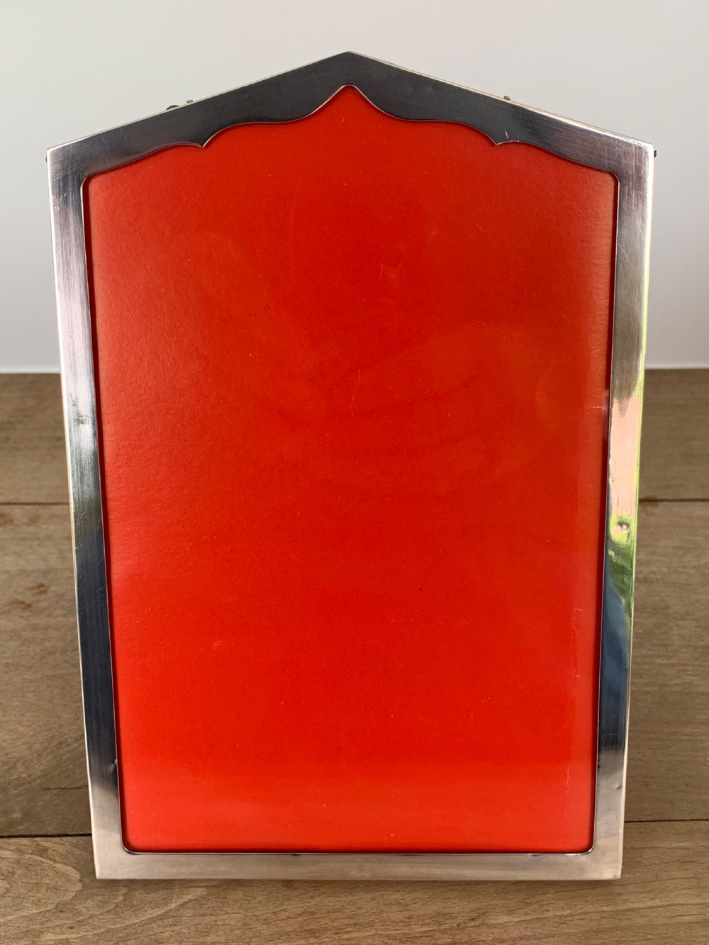 An Art Deco sterling silver picture frame featuring an arched top edge and a bright red background insert.