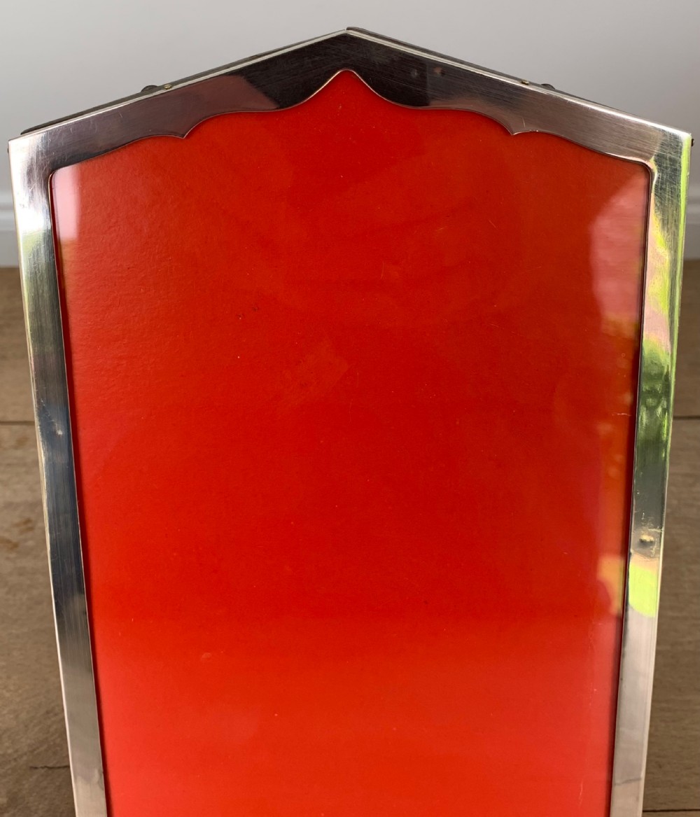 An Art Deco sterling silver picture frame featuring an arched top edge and a bright red background insert. View IV