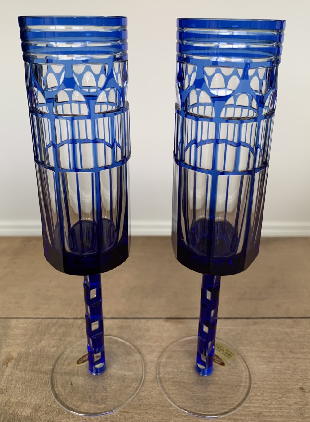 Pair of cobalt blue cut-to-clear crystal champagne flutes featuring geometric architectural patterns and notched square stems on round clear bases. View III