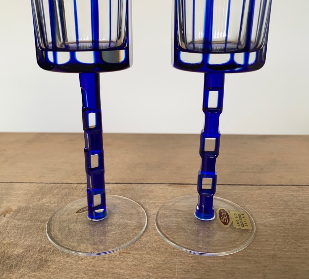 Pair of cobalt blue cut-to-clear crystal champagne flutes featuring geometric architectural patterns and notched square stems on round clear bases. View XIII