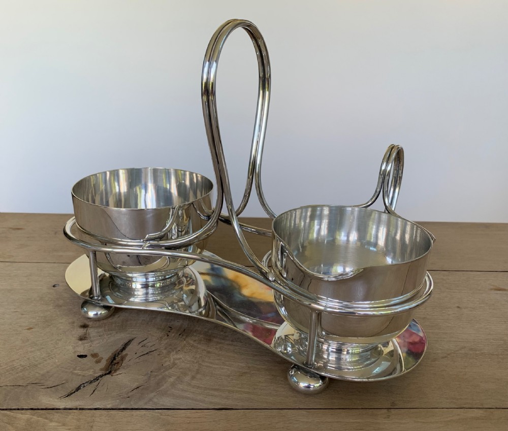 An Art Deco silver-plated sugar bowl and cream jug set within a fitted metal frame featuring a tall loop handle and ball feet. View II