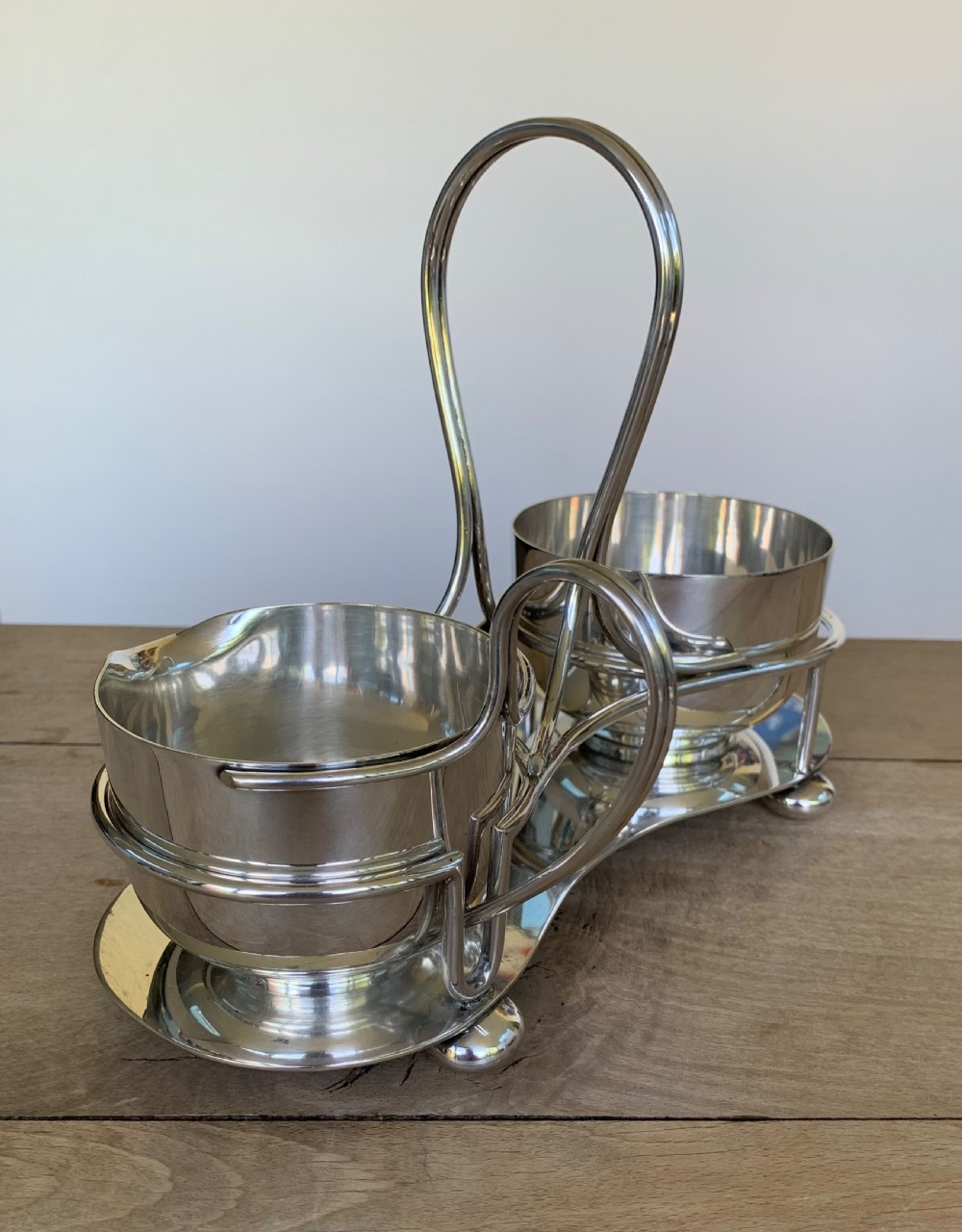 An Art Deco silver-plated sugar bowl and cream jug set within a fitted metal frame featuring a tall loop handle and ball feet. View IV