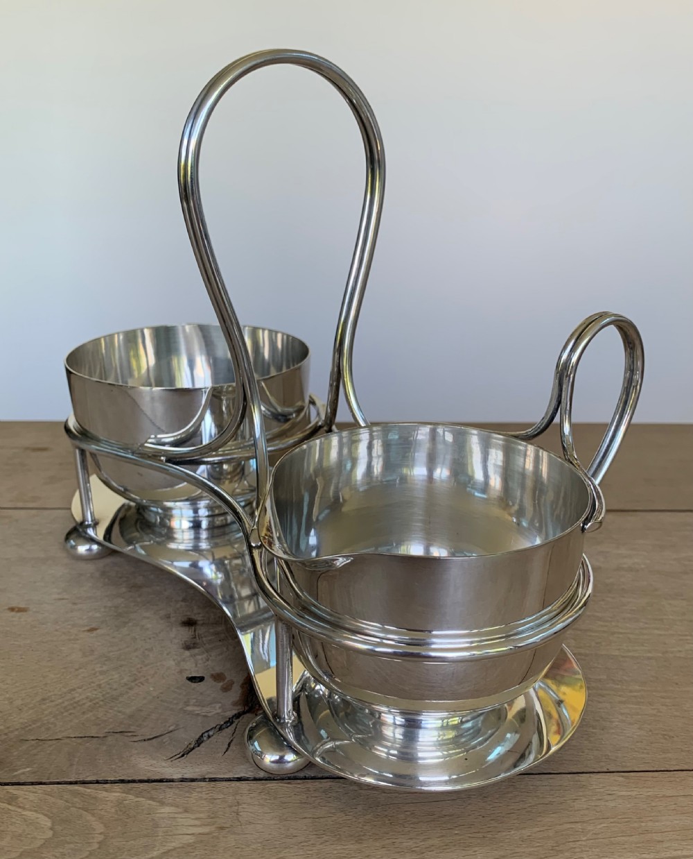 An Art Deco silver-plated sugar bowl and cream jug set within a fitted metal frame featuring a tall loop handle and ball feet. View V