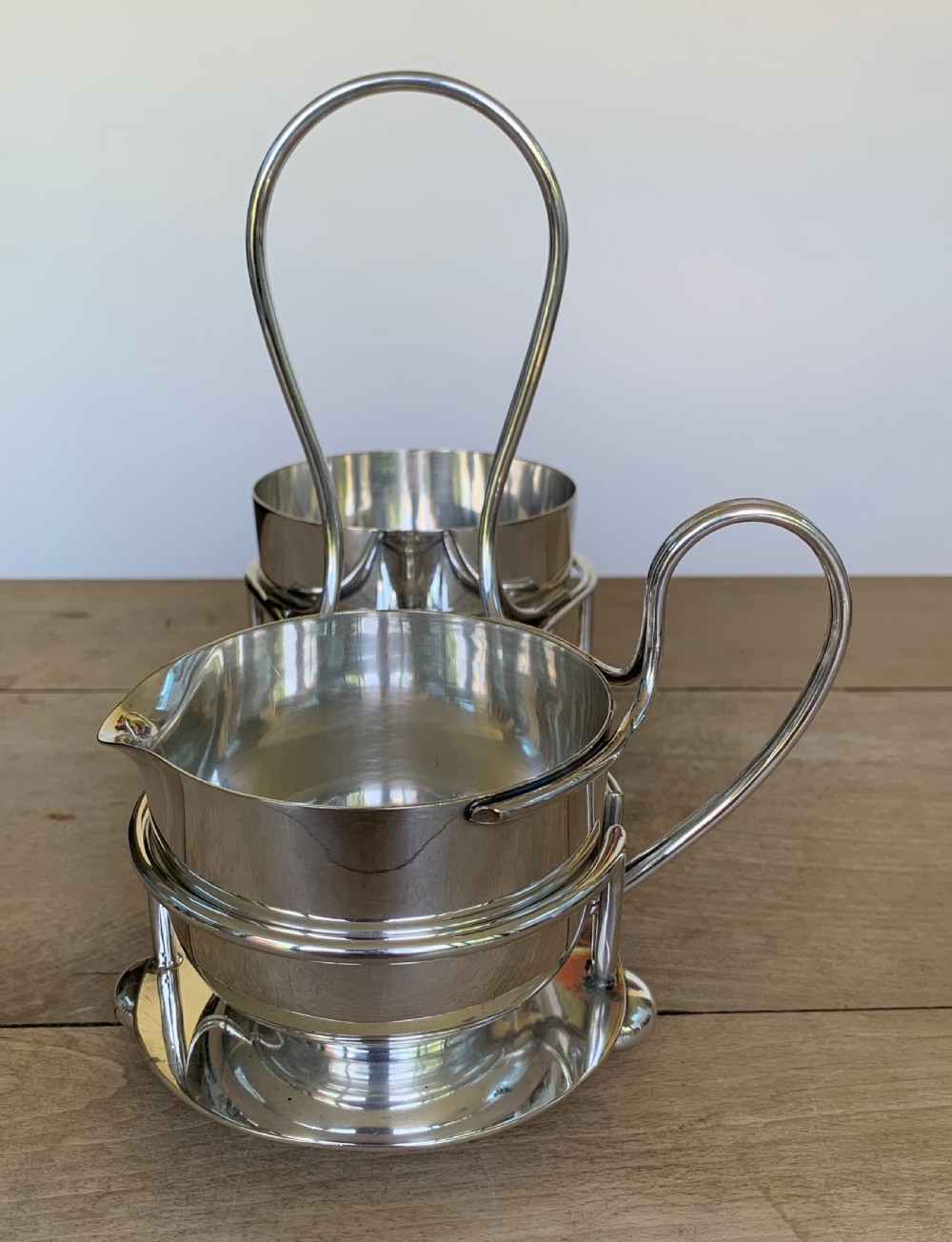 An Art Deco silver-plated sugar bowl and cream jug set within a fitted metal frame featuring a tall loop handle and ball feet. View VI