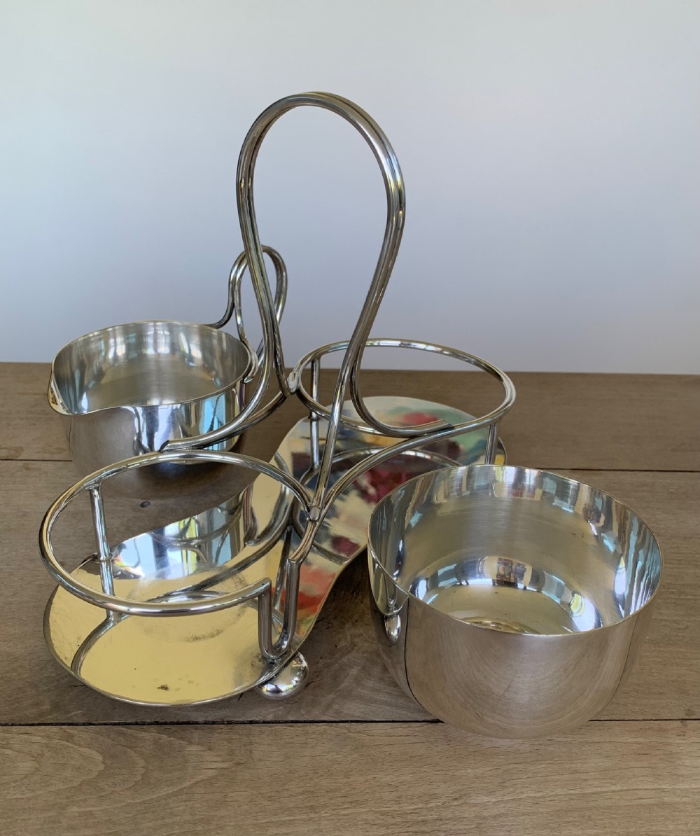 An Art Deco silver-plated sugar bowl and cream jug set within a fitted metal frame featuring a tall loop handle and ball feet. View VII