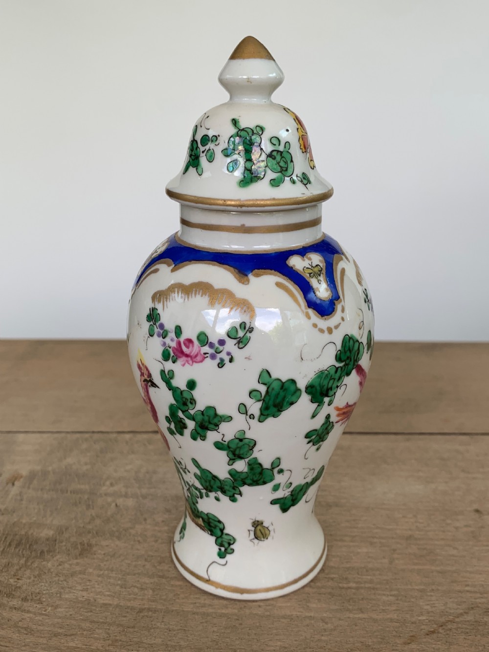 A white lidded porcelain vase decorated with a hand-painted pink exotic bird, green foliage, cobalt blue panels, and gilt trim. View III