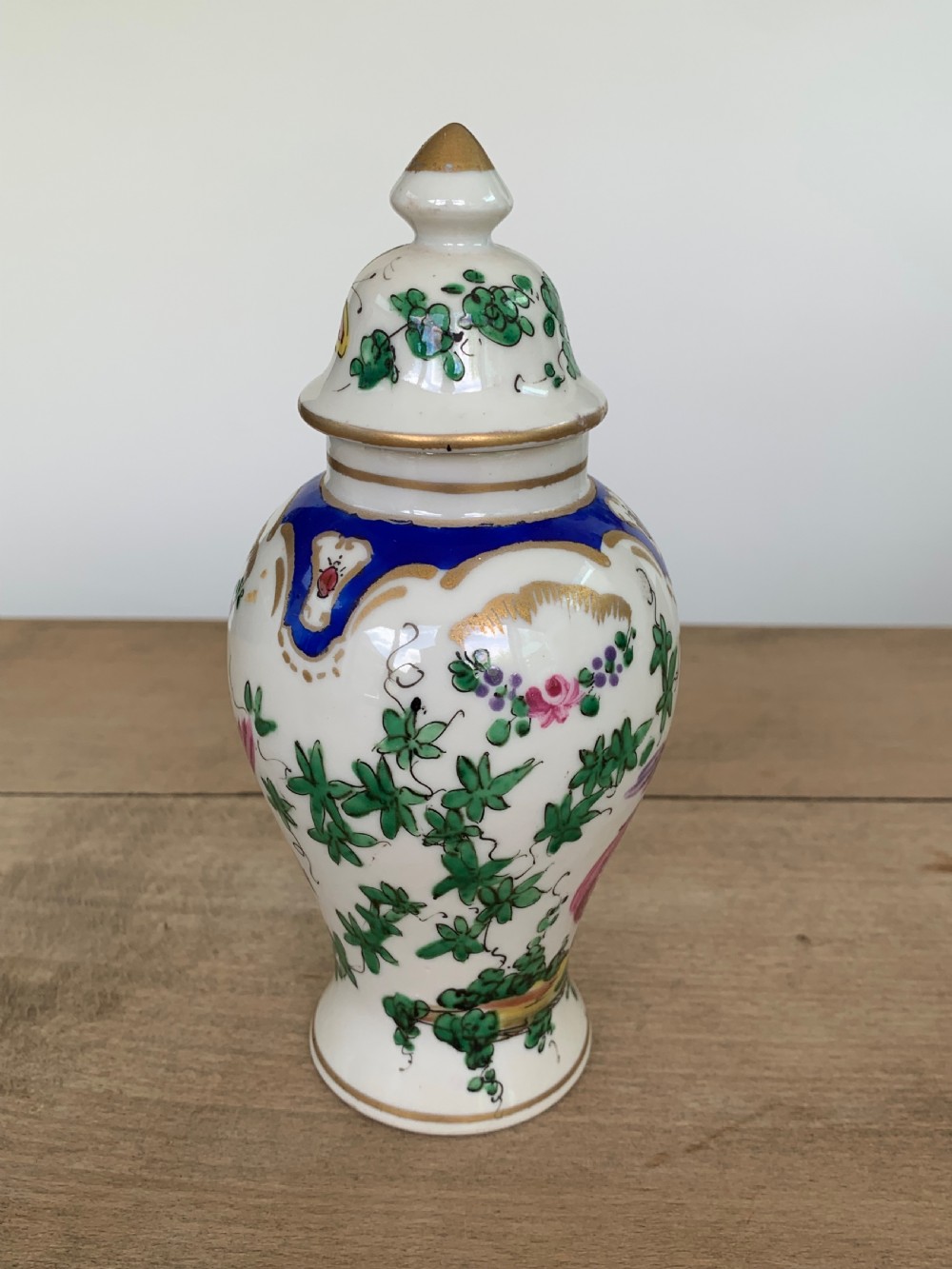 A white lidded porcelain vase decorated with a hand-painted pink exotic bird, green foliage, cobalt blue panels, and gilt trim. View IV