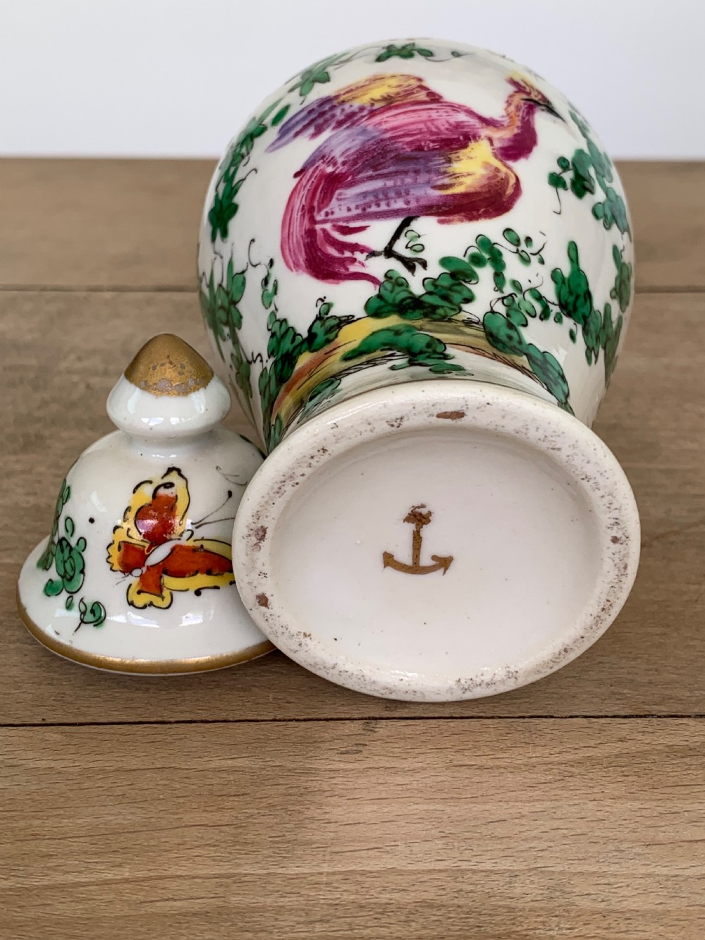 A white lidded porcelain vase decorated with a hand-painted pink exotic bird, green foliage, cobalt blue panels, and gilt trim. View VI