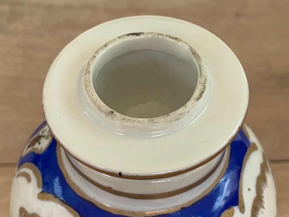A white lidded porcelain vase decorated with a hand-painted pink exotic bird, green foliage, cobalt blue panels, and gilt trim. View IX