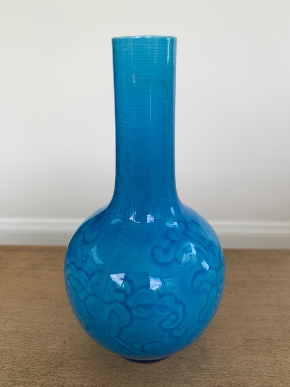 A turquoise blue Chinese porcelain bottle vase featuring a long cylindrical neck, rounded body, and incised peony motifs beneath a glossy glaze.
