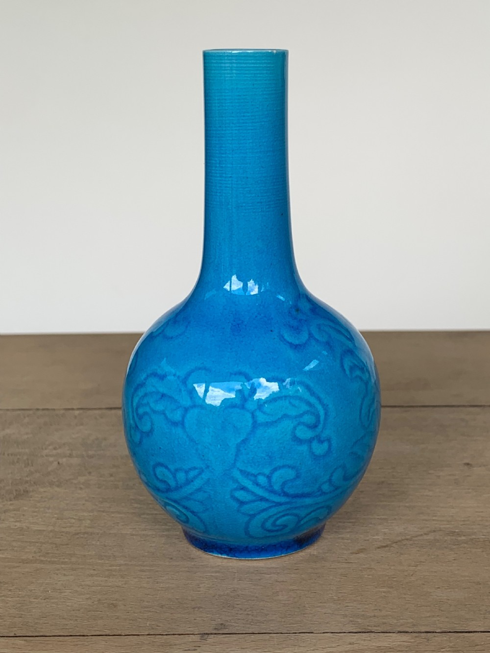A turquoise blue Chinese porcelain bottle vase featuring a long cylindrical neck, rounded body, and incised peony motifs beneath a glossy glaze. View II