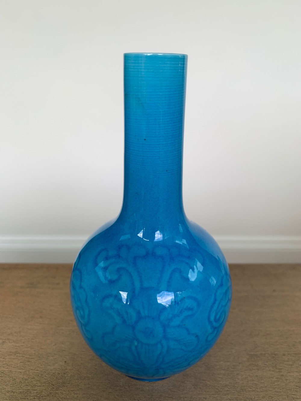 A turquoise blue Chinese porcelain bottle vase featuring a long cylindrical neck, rounded body, and incised peony motifs beneath a glossy glaze. View V