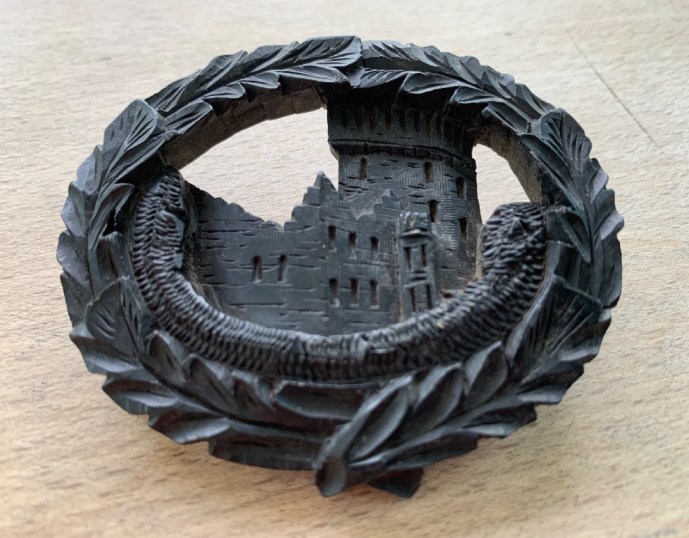 A hand-carved black bog oak oval brooch depicting Blarney Castle enclosed within a leaf border.