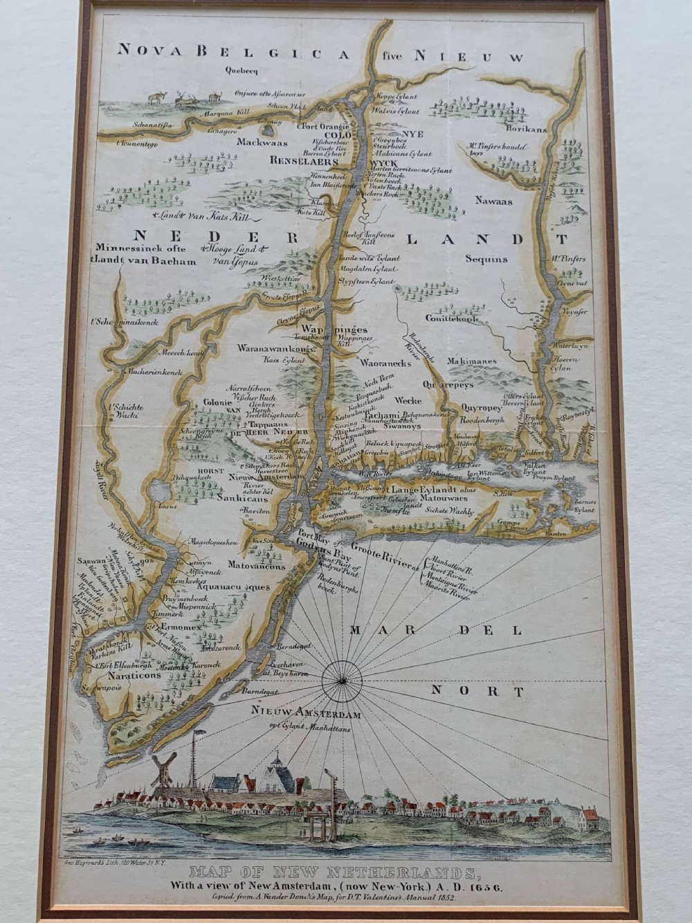 A framed antique map of New Netherlands featuring a detailed compass rose and an inset panorama illustration of early New Amsterdam along the bottom. View III