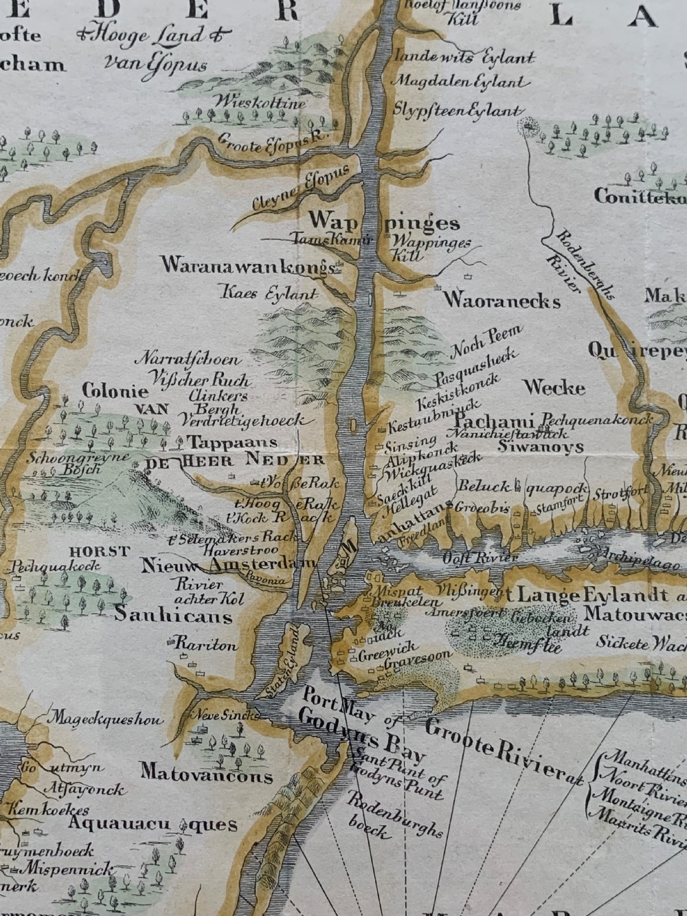 A framed antique map of New Netherlands featuring a detailed compass rose and an inset panorama illustration of early New Amsterdam along the bottom. View IV