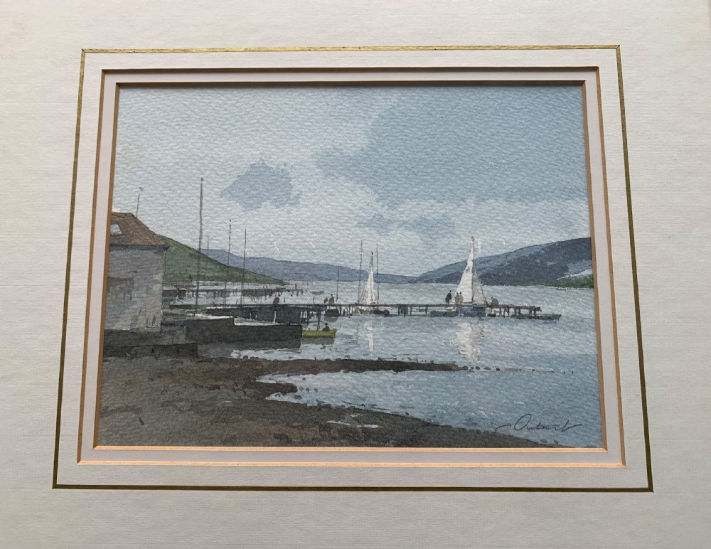 A framed watercolour painting by Stanley Orchart depicting sailboats, jetties, and stone buildings on the shore of Loch Earn under a cloud-filled blue sky.