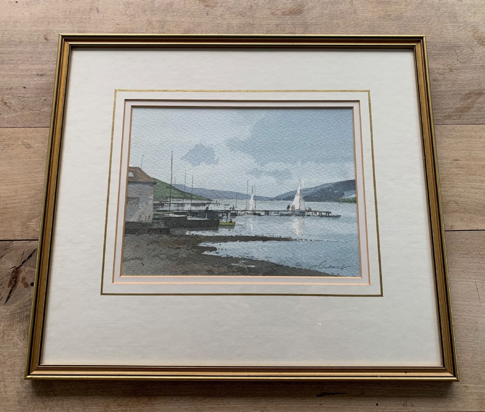 A framed watercolour painting by Stanley Orchart depicting sailboats, jetties, and stone buildings on the shore of Loch Earn under a cloud-filled blue sky. View III