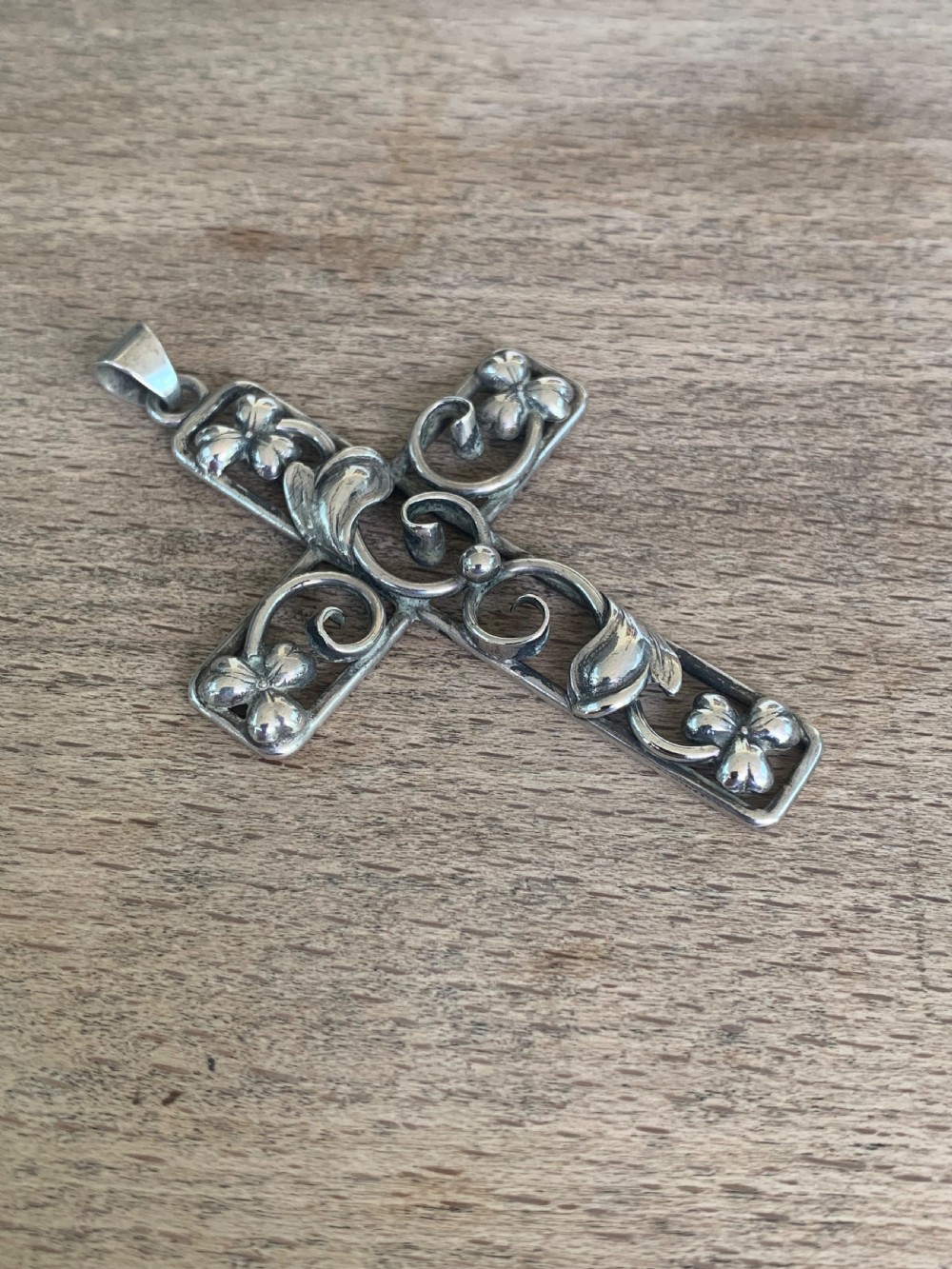 An antique silver cross pendant featuring openwork scrollwork and four-petal floral motifs at the terminals.
