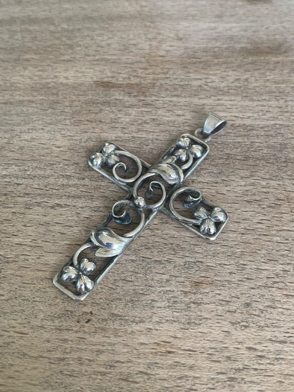 An antique silver cross pendant featuring openwork scrollwork and four-petal floral motifs at the terminals. View II