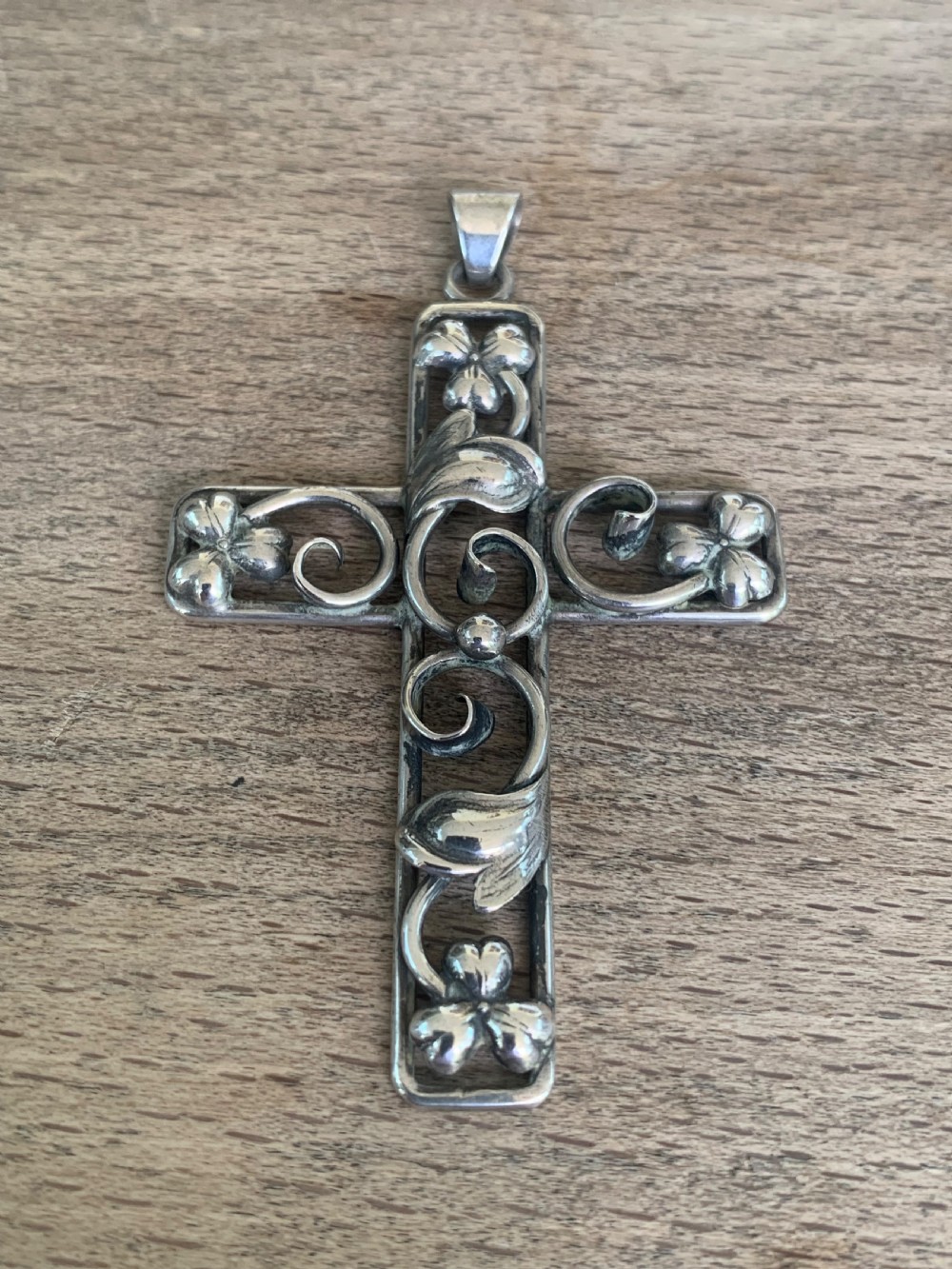 An antique silver cross pendant featuring openwork scrollwork and four-petal floral motifs at the terminals. View III